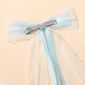 Detalle del clip de cocodrilo metálico en el lazo de encaje blanco y cinta azul para el pelo