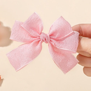 Detail of pink fabric bow hair clip with white piped edges and shimmer texture