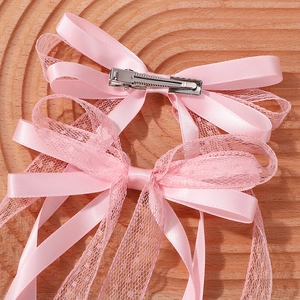 Détail de barrettes à nœuds roses en satin et dentelle avec pinces croco en métal