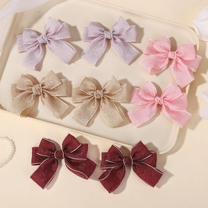 Detailed view of four colorful fabric bow clips with white piping on a beige tray