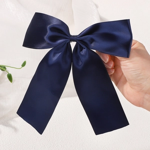 Close-up of a large navy blue satin bow hair clip with long ribbons and premium glossy finish