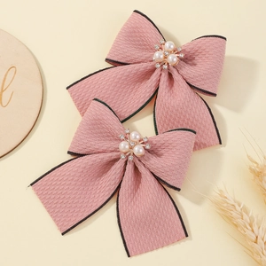 Close-up of pink fabric bow hair clips with white pearls and rhinestones on wood background