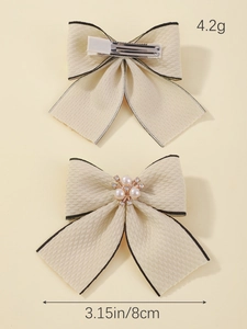 Detailed view of beige bow hair clip with black piping and pearl center decoration