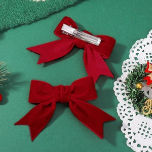 Pair of red velvet bow hair clips with long tails on festive green background