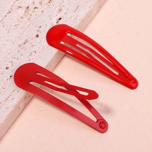 Detail view of two glossy bright red floral metal drop hair clips on a textured stone surface