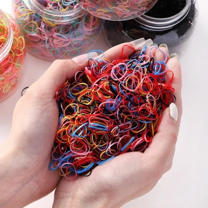 Macro shot of colorful high-elasticity hair ties being held next to clear storage jars