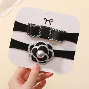 Detailed view of black camellia and bow nylon headbands with pearl accents on a display card