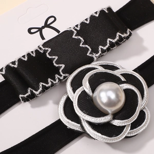 Detail shot of a black and white camellia hairband with a pearl center on a card