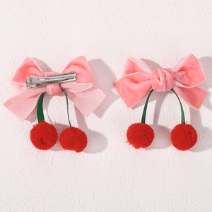 Détail des pinces à cheveux cerise en velours rose avec pompons rouges et clip en métal