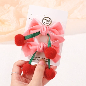 Détail de barrettes à nœuds en velours rose avec pompons rouges pour filles