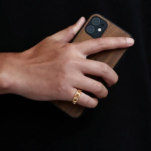 Nahaufnahme eines goldenen Rings im Panzerketten-Design an einem Finger vor dunklem Grund
