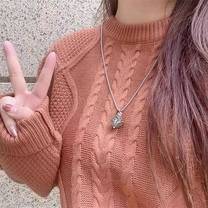 Detailed view of a silver cube pendant with vintage floral carvings on an orange sweater