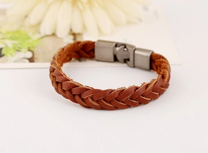 Détail d'un bracelet en cuir tressé marron avec fermoir en métal mat sur fond naturel