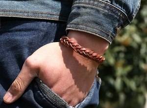 Gros plan d'un bracelet en cuir tressé marron porté avec une veste en jean