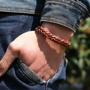 Bracelet unisexe en cuir tressé marron de style rétro porté au poignet sur un jean