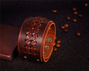 Detail of woven brown leather bracelet with adjustable metal snaps on dark texture