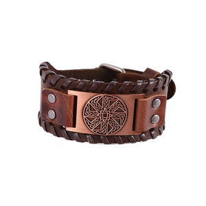 Close-up of wide punk leather bracelet with bronze metal emblem and woven edges