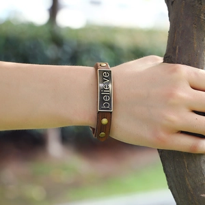 Vintage brown leather 'believe' bracelet with bronze rivets in a natural outdoor setting
