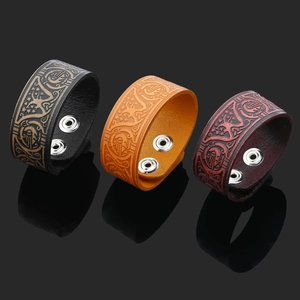 Detail view of wide leather Viking bracelets with embossed patterns in black and brown