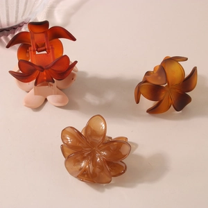 Three translucent amber and pink resin flower hair claws on a warm beige background
