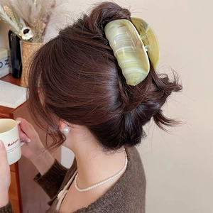 Macro detail of a large light green marble hair claw clip on a woman's bun hairstyle