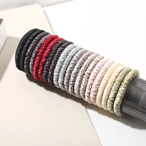 Detail shot of multicolor satin silk hair scrunchies set on a grey cylindrical display