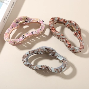 Three acetate hair claws in pink floral, tortoise shell, and blue marble cloud shapes