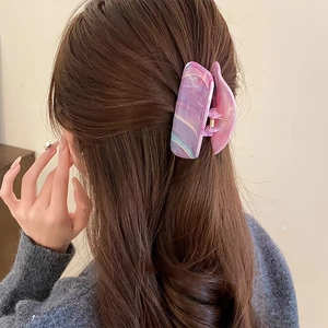Détail d'une pince à cheveux motif marbre sur cheveux ondulés avec ressort en métal