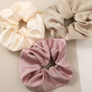 Detailed close-up of three soft satin scrunchies in cream, champagne and pink tones