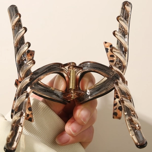 Hand holding a leopard print acetate claw clip showing strong golden metal spring and teeth