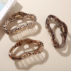 Three tortoiseshell acetate hair claws in leopard print on minimalist book aesthetic