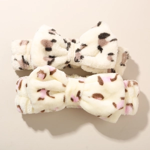Detail view of two plush leopard print bow headbands in soft cream and beige faux fur