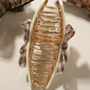 Detail view of acetate hair claw clip with amber resin finish and plaid bow fabric