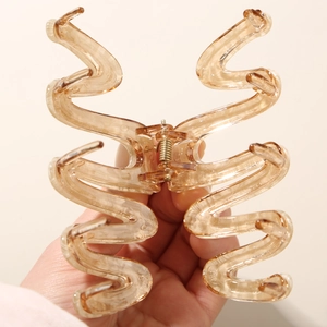 Large amber acetate hair claw clip with wave design held by hand for size reference