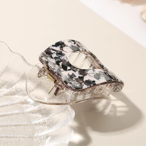 Detailed close-up of marble pattern acetate hair clip with golden metal spring on glass tray