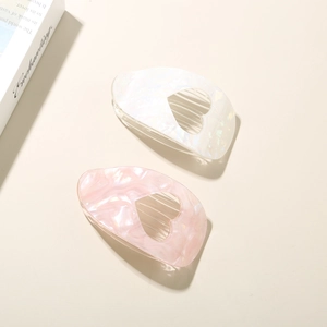 Close-up of pink marble and pearl heart-shaped acetate hair clips on a beige surface