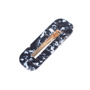 Detailed macro view of rectangular marble-textured acetate hair clip with golden metal clip