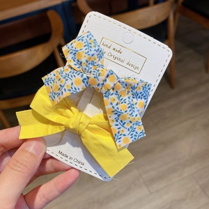 Detail of two-piece floral and yellow bow hair clips on a white display card