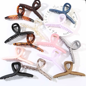 Set of eleven large matte and glossy hair claw clips in various elegant colors on a white plate