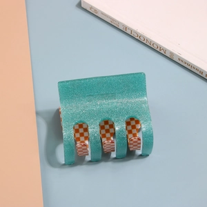 Detail of teal glitter hair claw clip with orange checkered inner pattern and metal spring