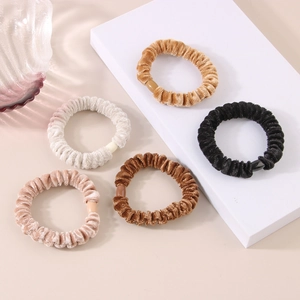 Set di cinque elastici per capelli in velluto dai toni caldi su un piedistallo moderno