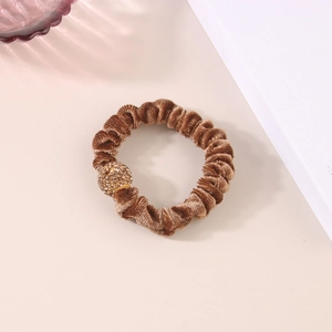 Dettaglio di un elastico per capelli in velluto marrone con una sfera dorata con strass lucidi