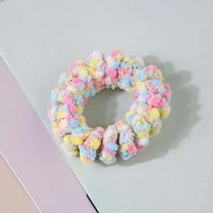 Gros plan sur un élastique à cheveux en peluche pastel avec des pompons colorés