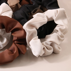 Detail of satin scrunchies showing pleated texture and glossy finish in neutral tones