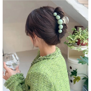 Detail of a large bean green hair claw clip with pearl finish on a woman's bun hairstyle
