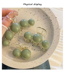 Close-up of three olive green acrylic hair claws in various sizes on a white ceramic plate