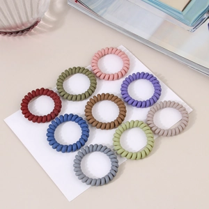Détail de neuf élastiques à cheveux spirales mats de couleurs assorties sur fond neutre