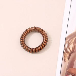 Gros plan sur un élastique spirale bronze métallique sur fond beige épuré