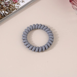Gros plan d'un élastique spirale gris mat pour cheveux sur un fond minimaliste doux