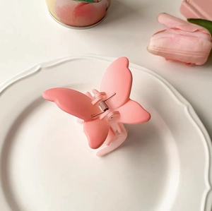 Matte pink butterfly hair claw clip for women on a decorative ceramic white plate